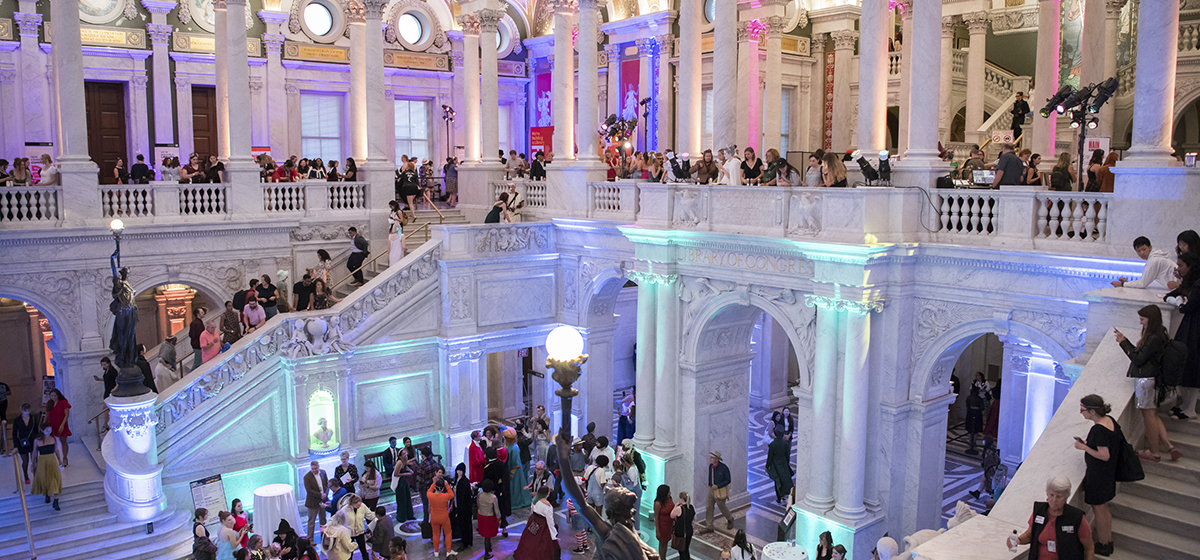 A view of the Great Hall of the Thomas Jefferson Building of the Library of Congress, with many people shown enjoying the beautiful architecture in the hall, on the stairs and in the gallery above